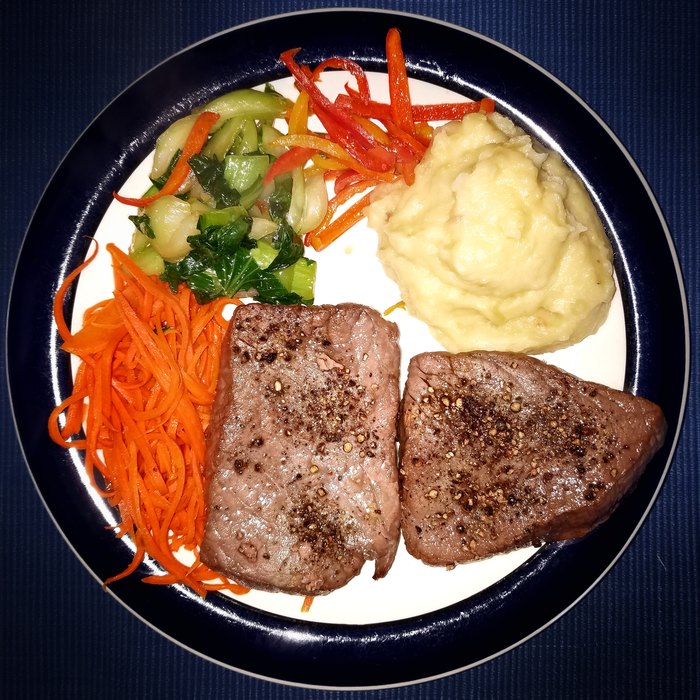 Plato redondo visto desde arriba con carne de res molida cocida, cubos de batata naranja y arvejas verdes, sobre fondo azul rey